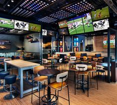 a sports bar with multiple tables and stools in front of large screens on the wall