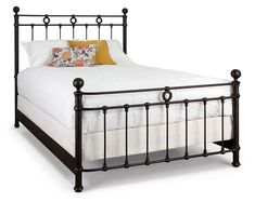 a black metal bed frame with white sheets and pillows on top of it, against a light wood floor