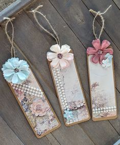 three bookmarks with flowers on them hanging from string and wood planks in front of a wooden floor