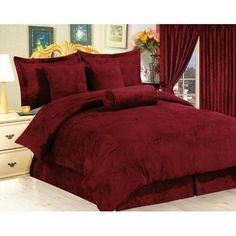 a red comforter set on a bed in a room with hardwood floors and windows