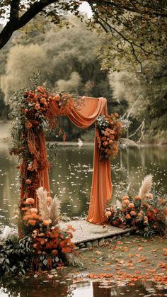 an outdoor wedding setup with orange draping and flowers on the water's edge