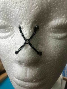 a white mannequin head with black beads and a cross on it's forehead