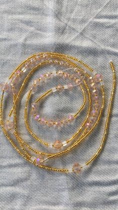 a gold chain with pink beads on it and some other items in the background that are laying on top of a blue cloth