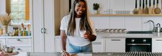 a woman standing in a kitchen next to a counter with food on it and smiling at the camera