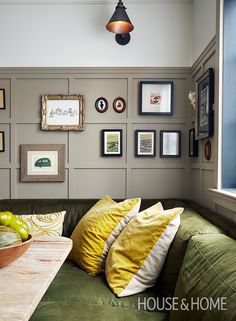 a green couch with yellow pillows and pictures on the wall