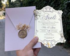 a person holding up a wedding card with a medallion on the front, and an envelope in the back