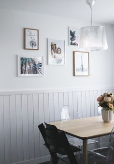 a dining room table with chairs and pictures on the wall above it, along with vases filled with flowers