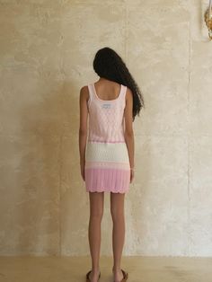 a woman standing in front of a wall wearing a pink and white knitted dress