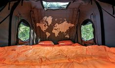 the inside of a tent with an orange comforter and two windows that look out onto trees