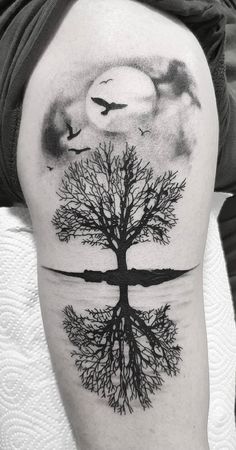 a black and white photo of a tree with birds flying in the sky above it