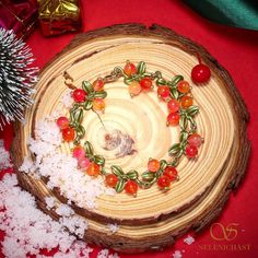 a wreath made out of cherry tomatoes and green leaves on a piece of wood surrounded by snow