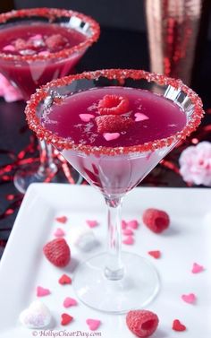 two martinis with raspberries in them on a white plate and pink confetti