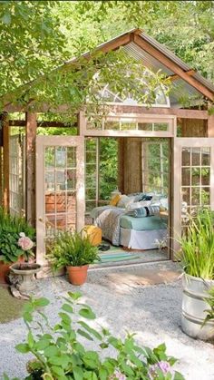 a garden shed with lots of potted plants and flowers in the foreground, surrounded by greenery