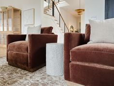 a living room with two brown chairs and a stair case in the back ground area