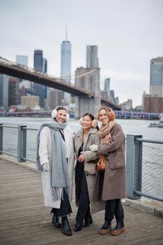 three women standing next to each other in front of a bridge and cityscape