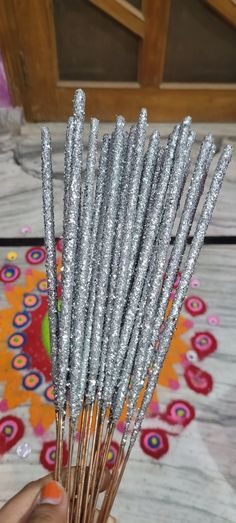 a person holding up some silver sparkle sticks on top of a rug with flowers in the background