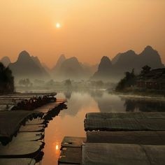 boats are lined up on the water in front of mountains and foggy sky at sunset