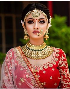 a woman in a red and gold bridal outfit with jewelry on her neck, nose ring