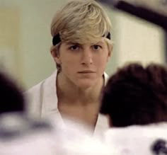 a man with blonde hair is looking at another person's reflection in the mirror