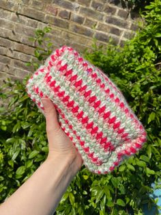 a hand holding up a crocheted red and white purse