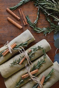 napkins tied with twine and rosemary are sitting on a wooden table next to some leaves