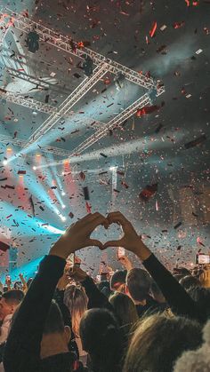 two hands in the shape of a heart at a concert with confetti falling from overhead