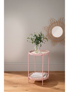 a small pink table with flowers on it and a mirror in the corner behind it