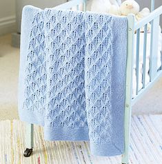 a blue crocheted baby blanket hanging from the side of a crib