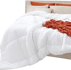 a white bed with an orange blanket and pillows on it's headboard, in front of a white background