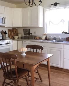 a kitchen with white cabinets and wooden table in the center, an oven on the far wall