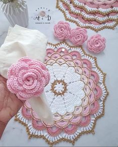 crocheted doily and napkins with pink flowers on them are being held by someone's hand