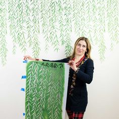 a woman standing in front of a wall holding up a painting