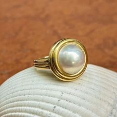 New, but old pieces, never worn, recently acquired from a premiere jeweler located in Minneapolis, MN for many years- a rare opportunity. 18KT yellow gold genuine, double bezel, round, mabe pearl ring Size 6.50 Sizable by us for a fee or your local jeweler Weight: 12.2 grams Band width: 3mm in back 11.50~12mm round mabe pearl Stamped 18k Classic Cabochon Pearl Ring For Formal Occasions, Gold Oval Cabochon Pearl Ring, Classic Formal Pearl Ring With Cabochon, Oval Gold Pearl Ring With Cabochon, Anniversary Yellow Gold Pearl Ring With Cabochon, Elegant Round Cabochon Pearl Ring, Classic Round Pearl Ring With High Luster, Classic Gold Pearl Ring With High Luster, Formal Cabochon Pearl Ring