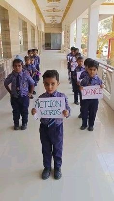 several children holding signs in the hallway of a school building that says action words written on them