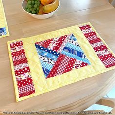 two quilted placemats sitting on top of a wooden table next to a bowl of fruit