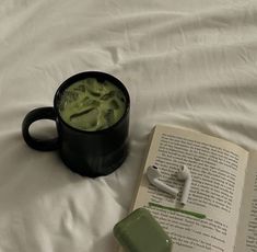 an open book sitting on top of a bed next to a cup of green liquid