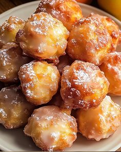 a white plate topped with donuts covered in powdered sugar next to oranges