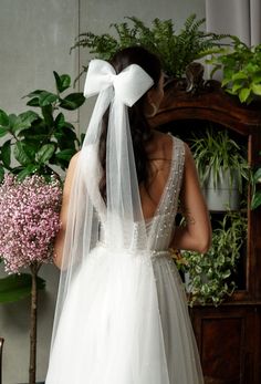 the back of a bride's wedding dress with a white bow on her head