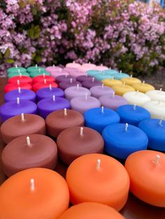 many different colored candles sitting on top of a table next to some pink and purple flowers