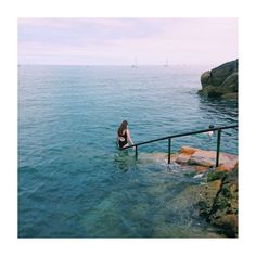 a woman sitting on top of a metal railing next to the ocean