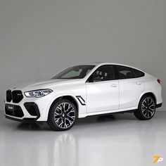 a white bmw suv is parked in a room with gray walls and flooring on the side