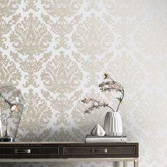 two vases with flowers on a table in front of a wallpapered background