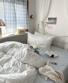 an unmade bed sitting next to a window with white curtains and flowers on it