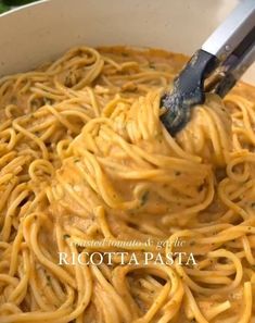 a bowl filled with pasta and sauce being stirred by a spatula