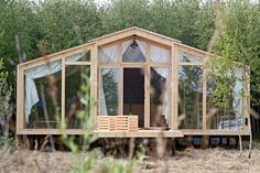 a small house made out of wood and glass in the middle of a field with lots of trees