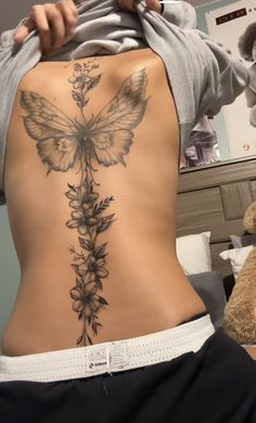 the back of a woman's stomach with a butterfly and flowers tattoo on it