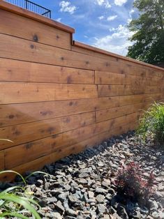 the side of a wooden fence with rocks and plants growing on it's sides