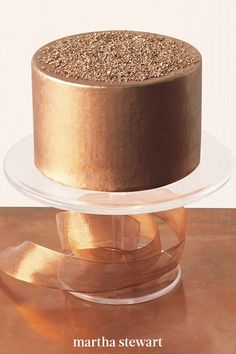 a chocolate cake with gold sprinkles is on a clear plate next to a brown ribbon