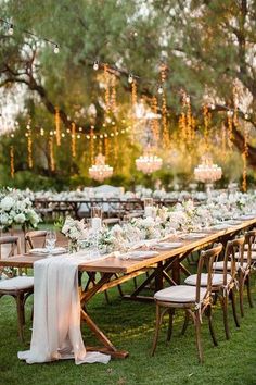 a long table with white flowers and candles is set up for an outdoor wedding reception