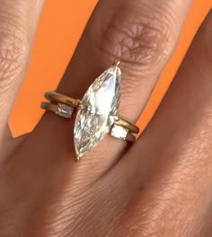 a woman's hand with an engagement ring on top of her finger, in front of an orange background